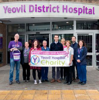Leonardo colleagues stand outside Yeovil Hospital and hold sign that reads, "Breast Cancer Unit Appeal - Yeovil Hospital Charity"