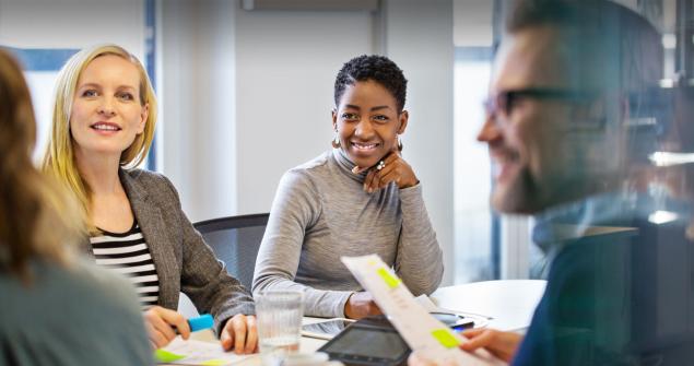 Two women smile while sitting at boardroom table