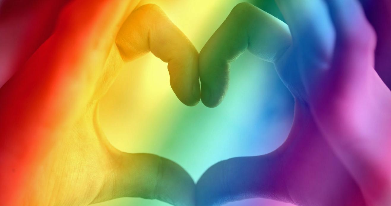 Heart made by two hands with rainbow wash over it
