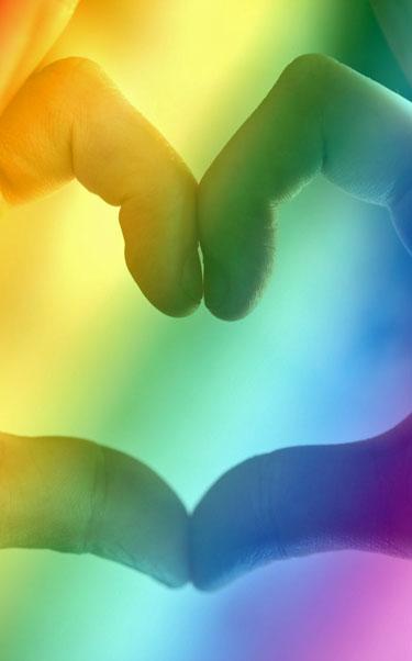 Heart shape formed by hands through LGBTQ+ colours