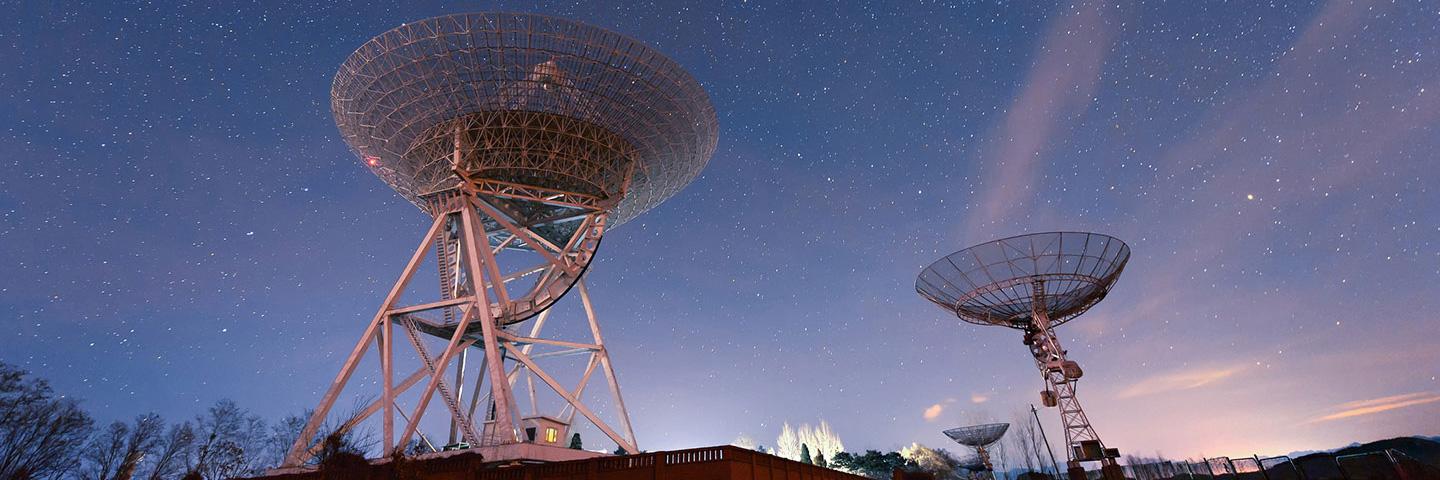 A collection of satellite ground stations pointing towards the sky set against a clear starry night