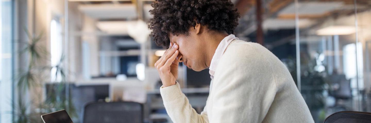 Mixed race man sits at his office desk in a state of anxiety, while covering his eyes