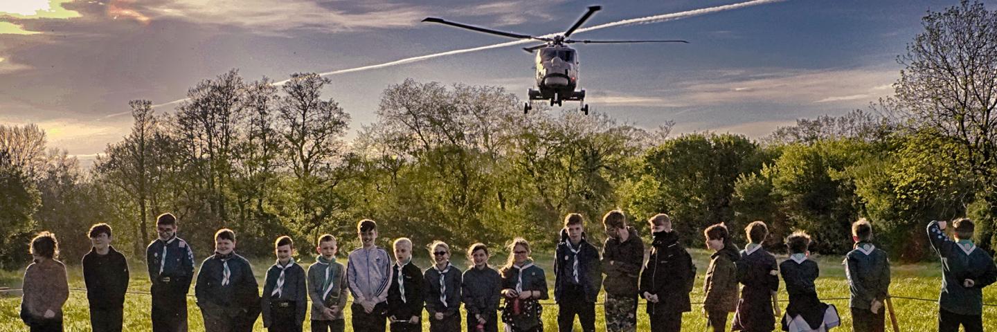 An AW149 helicopters flies over a group of scouts
