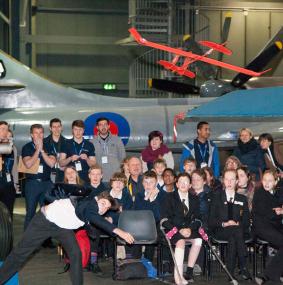 A boy throws a Flying Start Challenge model aeroplane, while a crowd of students and Leonardo STEM ambassadors watch on