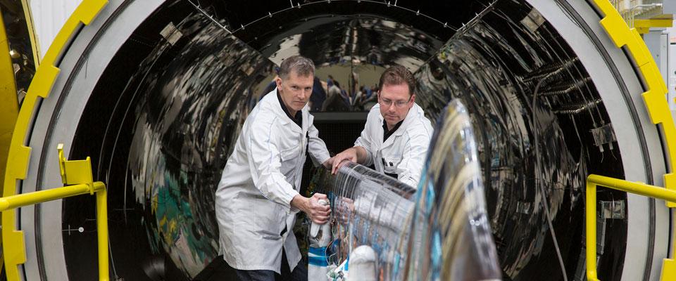 Two older white men in lab coats work on aircraft