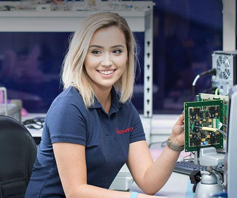Young white female engineer smiles while working with circuit board