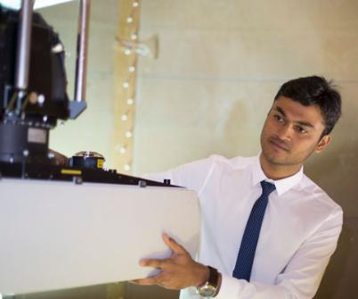 Young Asian male engineer wearing shirt and tie holds onto machinery