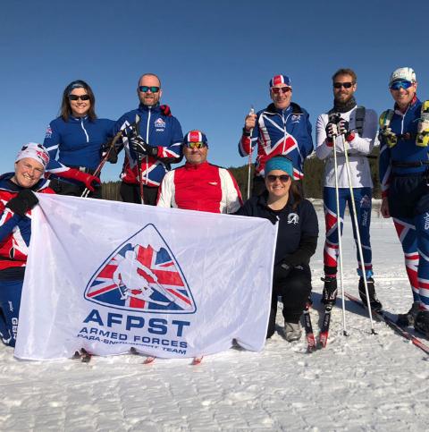 Group of Armed Forces Para Snow Team male and female skiers holding the charity flag in a snow landscape