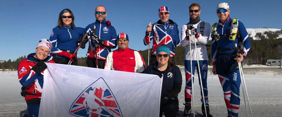Group of Armed Forces Para Snow Team male and female skiers holding the charity flag in a snow landscape
