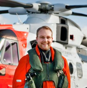 Male Leonardo employee in aircrew attire in front of the Norwegian AW101 Search and Rescue helicopter