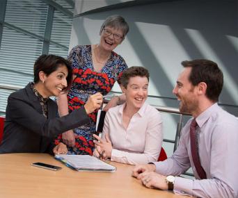 Colleagues of different ages and ethnicities laugh around meeting room table