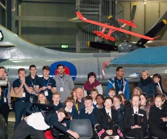 A boy throws a Flying Start Challenge model aeroplane, while a crowd of students and Leonardo STEM ambassadors watch on