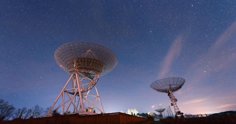 A collection of satellite ground stations pointing towards the sky set against a clear starry night