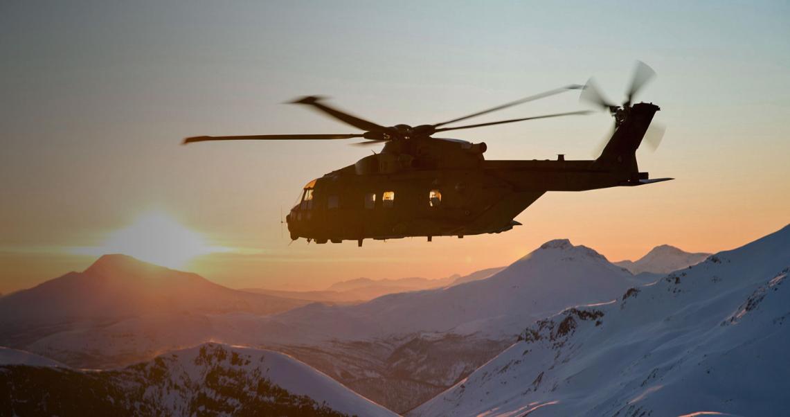 AW101 Merlin flying over snow-topped mountain peaks at sunset