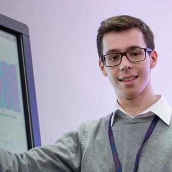 Young white male in glasses points to whiteboard and smiles