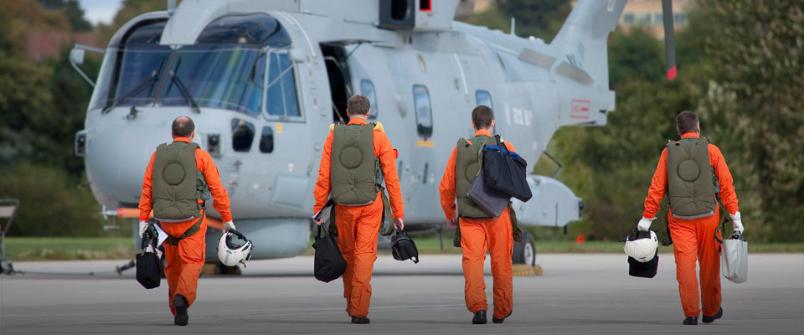 Four male helicopter pilots in orange jumpsuits walk towards AW101, holding helmets