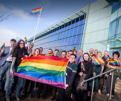 Group of people outside of the Edinburgh office holding LGBT rainbow flags