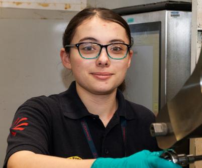 Young female engineer in glasses smiles and works on machinery